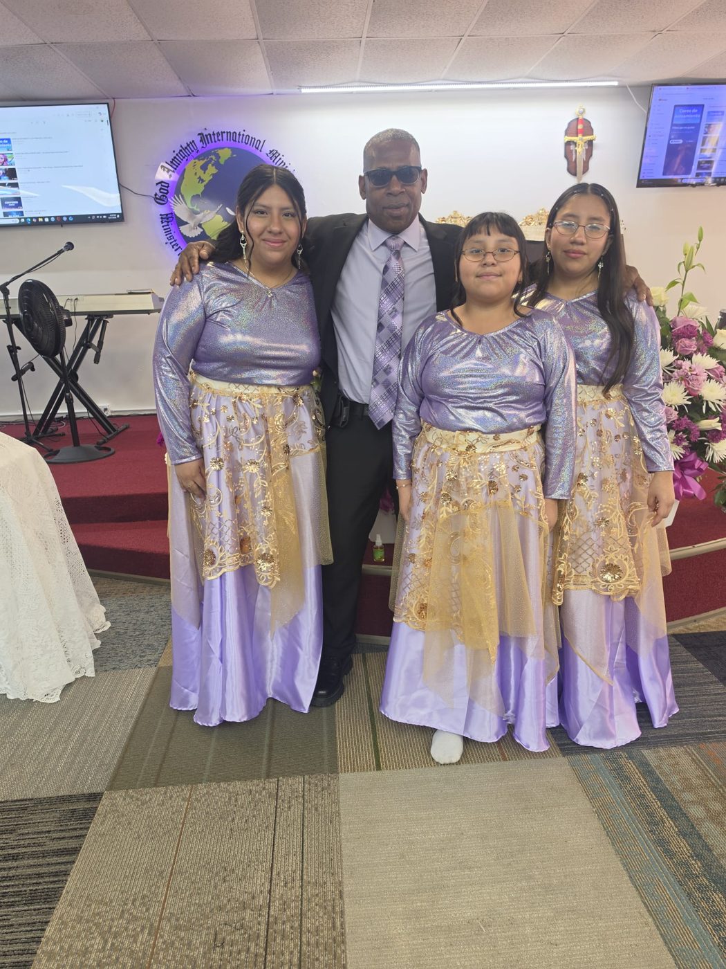 Tres jóvenes del ministerio de danza con vestidos lila y dorado junto a un ministro